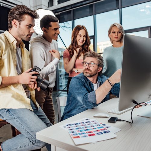 selective focus of creative director looking at happy assistants in photo studio